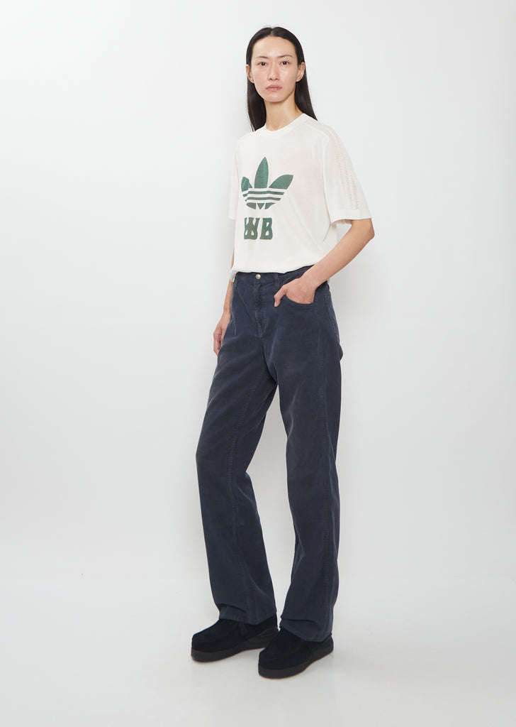 A full-length side view of a model wearing Visvim navy Fluxus Boot Cut Pants.