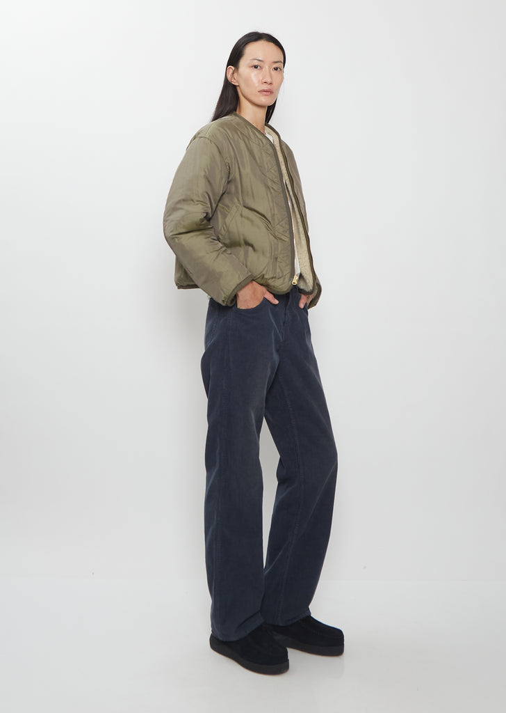 A full-length side view of a model wearing the Visvim Liner Down Jacket in ivory with dark trousers.