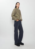 A full-length side view of a model wearing the Visvim Liner Down Jacket in ivory with dark trousers.