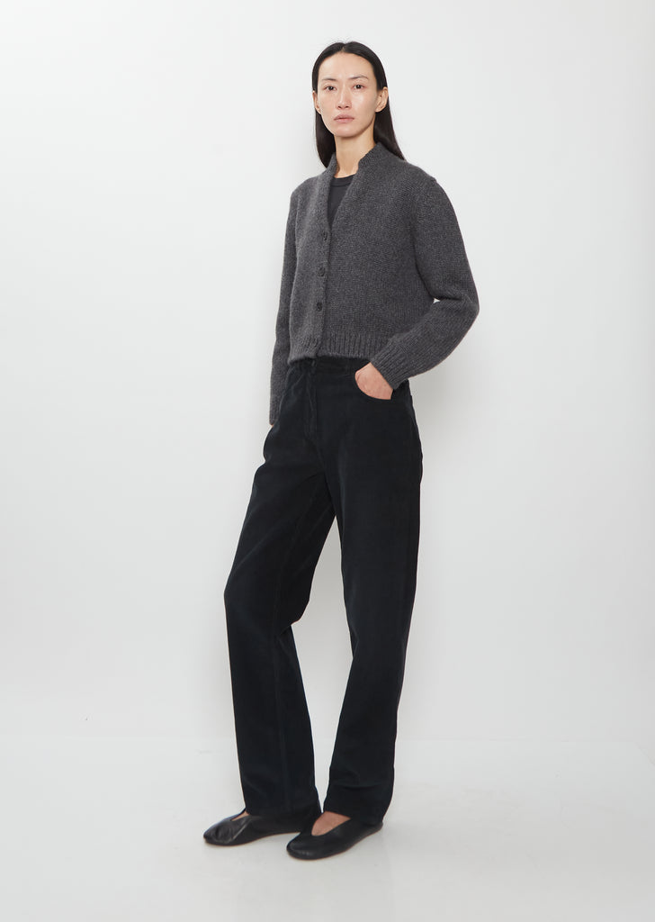 A full-length view of the Duvan Cotton Corduroy Pant in faded black worn with a grey cardigan.