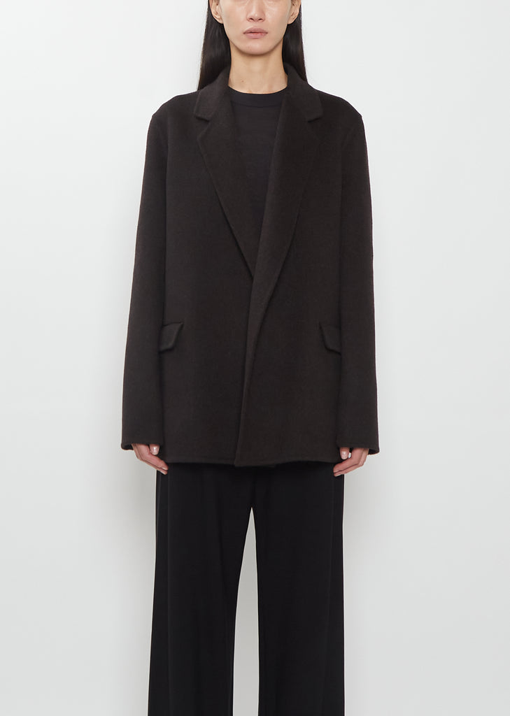 Front view of a model wearing The Row dark brown Cinna Cashmere Jacket and black trousers.