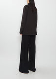Rear view of the dark brown The Row Cinna Cashmere Jacket paired with black trousers.