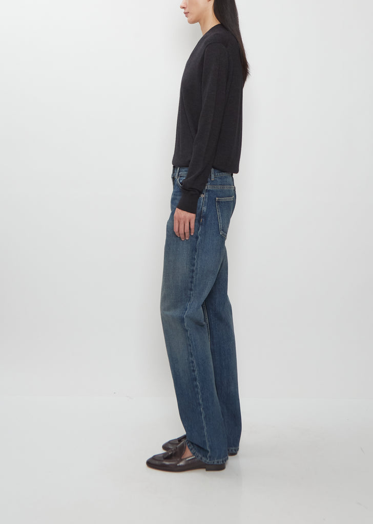 Side view of a model wearing The Row medium indigo Dinni Cotton Jeans with a straight-leg cut.