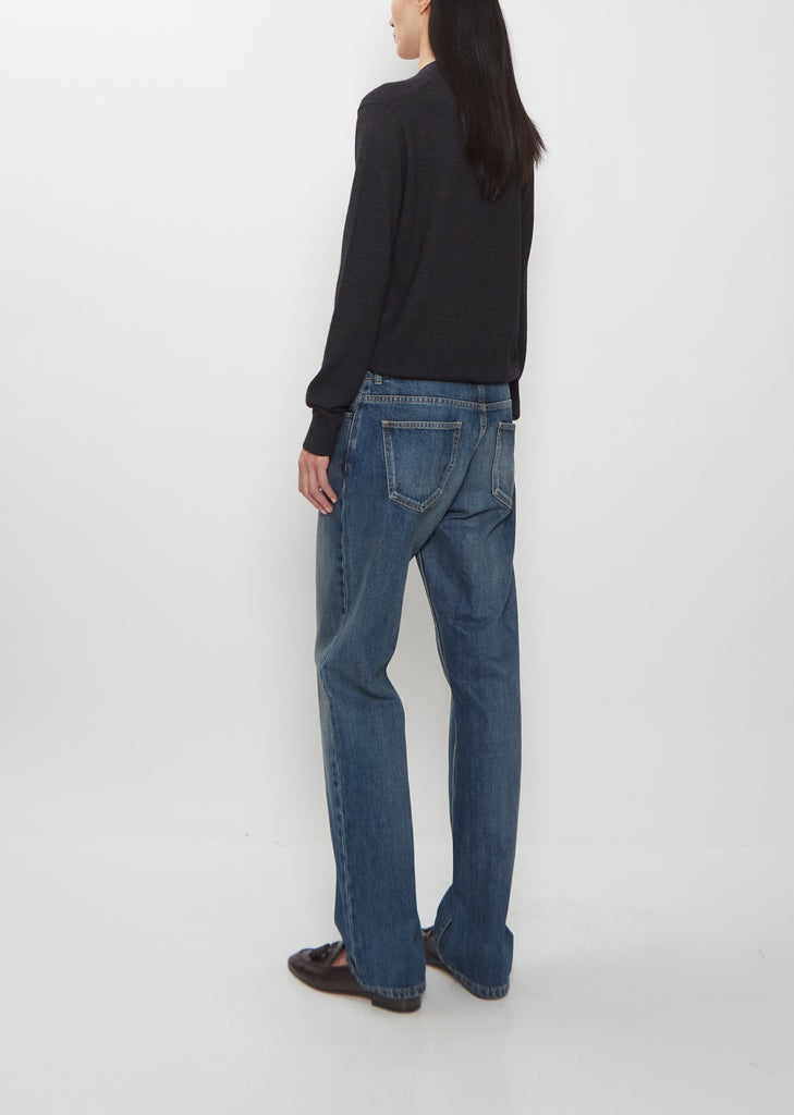 Rear view of a model wearing The Row Dinni Cotton Jean in medium indigo with a dark sweater.