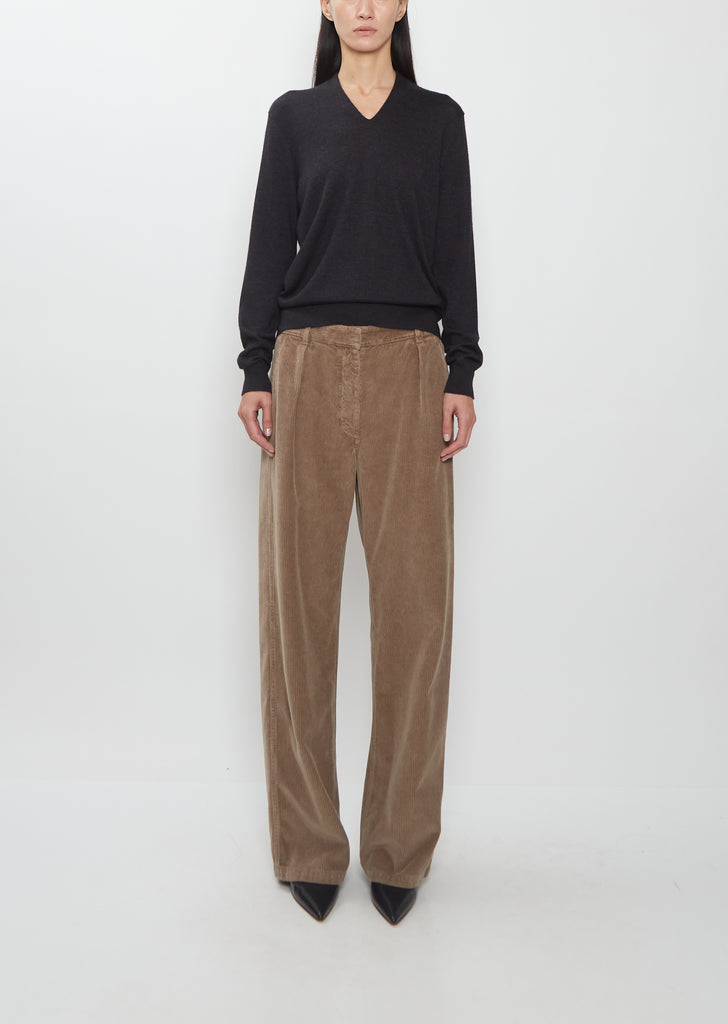 Front view of The Row Adler Cotton Corduroy Pant in faded sepia, worn with a black V-neck sweater.