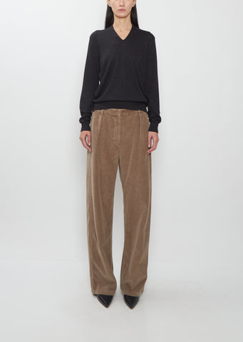 Front view of The Row Adler Cotton Corduroy Pant in faded sepia, worn with a black V-neck sweater.