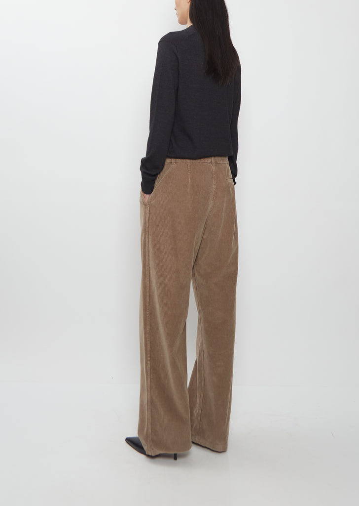 Back view of a model wearing The Row Adler Cotton Corduroy Pant in faded sepia with a black top.