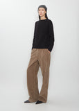 Full view of a model wearing The Row Quors Cashmere Hat in charcoal melange, paired with a black sweater and brown corduroy trousers.