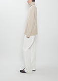 Side view of The Row Stepny Wool Cashmere Top in sand beige worn with white trousers.