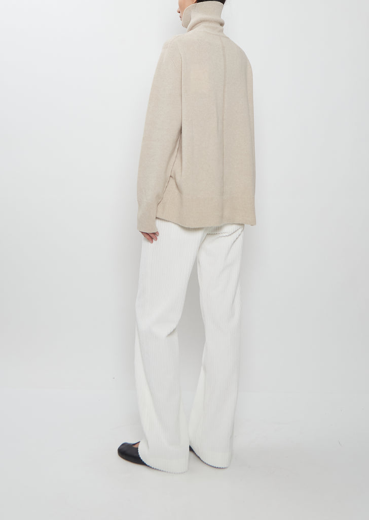 Rear view of a model wearing The Row Stepny Wool Cashmere Top in sand beige with white pants.