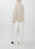 Rear view of a model wearing The Row Stepny Wool Cashmere Top in sand beige with white pants.