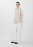 Full view of the The Row Stepny Wool Cashmere Top in sand beige worn with white trousers.