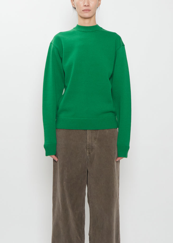 Front view of a model wearing the green Auralee super fine wool knit pullover and brown trousers.
