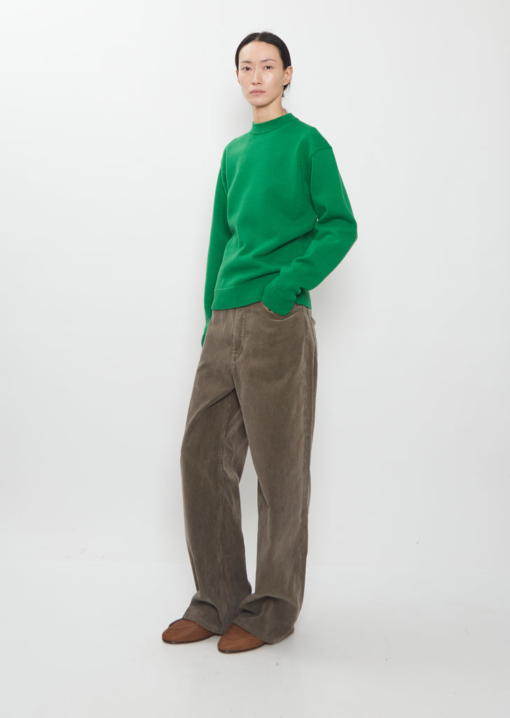 Full-body view of the Auralee Super Fine Wool Knit Pullover in green paired with brown corduroy trousers.