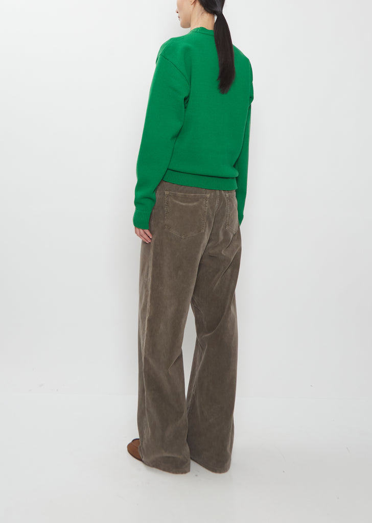 Rear view of a model wearing the Auralee Super Fine Wool Knit Pullover in green with grey trousers.