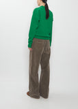 Rear view of a model wearing the Auralee Super Fine Wool Knit Pullover in green with grey trousers.