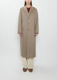 Front view of a model wearing the Auralee cashmere moleskin long coat in light brown over cream trousers.