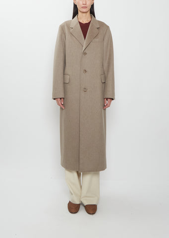 Front view of a model wearing the Auralee cashmere moleskin long coat in light brown over cream trousers.