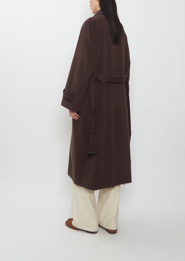 Person seen from behind wearing a long brown Super Fine Wool Mosser Soutien Collar Coat with wide cream-colored trousers.