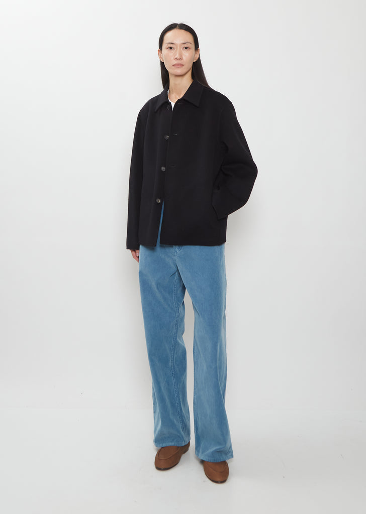 A person wearing a black Super Fine Wool Melton Hand Sewn Blouson over a white shirt, blue trousers, and brown shoes.
