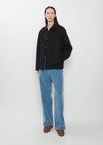 A person wearing a black Super Fine Wool Melton Hand Sewn Blouson over a white shirt, blue trousers, and brown shoes.
