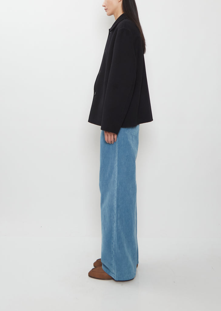 Side profile of a person in a Super Fine Wool Melton Hand Sewn Blouson, wide-leg blue jeans, and brown shoes.