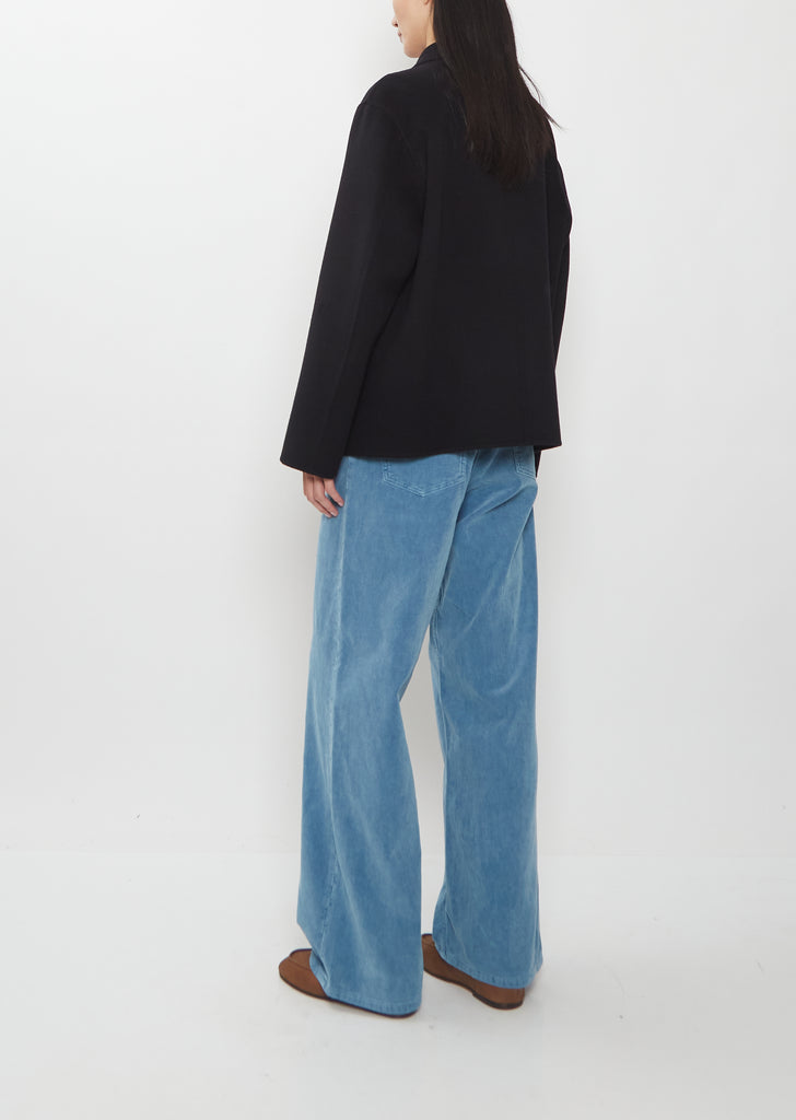 A person from behind wearing a black Super Fine Wool Melton Hand Sewn Blouson, wide-leg blue jeans, and brown shoes.