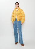 A person wears a yellow Super Light Nylon Ripstop Down Blouson, white t-shirt, blue trousers, and brown shoes.