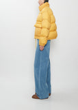 A person wearing a bright yellow, boxy Super Light Nylon Ripstop Down Blouson and loose-fitting blue trousers.