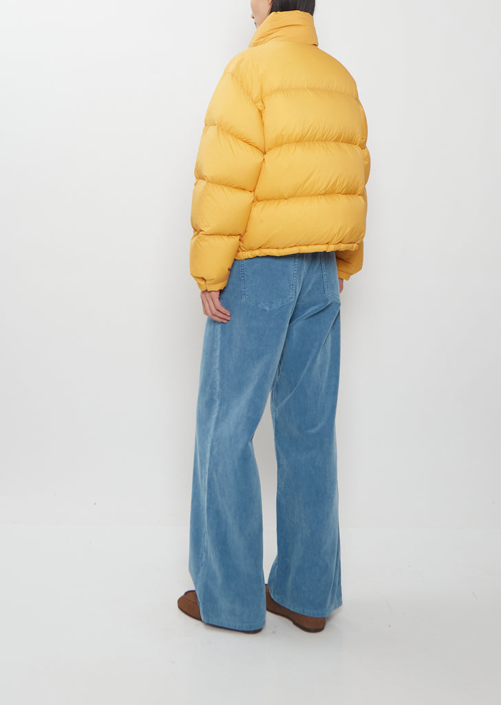 A person wearing a yellow Super Light Nylon Ripstop Down Blouson and blue wide-leg trousers.
