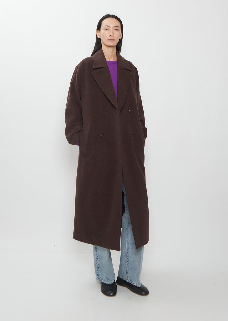 A model wears a dark brown Super Fine Wool Mosser Double Breasted Coat over a purple sweater and light blue jeans.